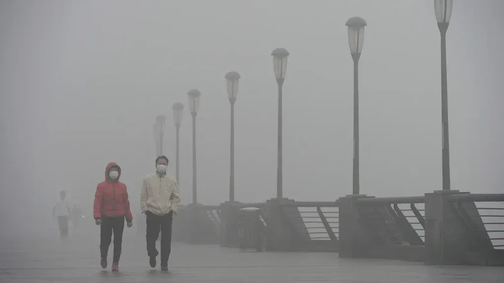 Two people wearing face masks walking along a waterfront in heavy smog